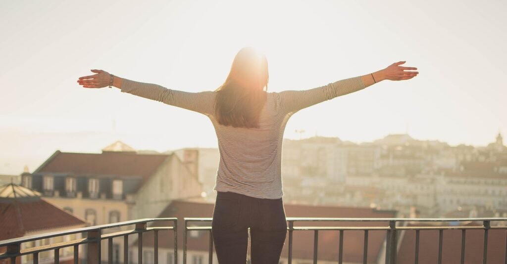 A woman at the Balcony raising her hands, standing in front of the morning light.